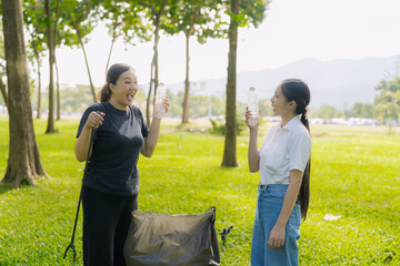 Two Asian women are picking up litter on the lawn in a park, participating in a daytime environmental cleanup.