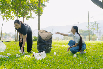 Two Asian women are picking up litter on the lawn in a park, participating in a daytime environmental cleanup.