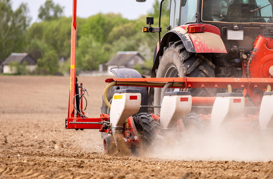 Tractor seeding soil with planter in agricultural field. Tractor drilling seeding crops at farm field. Agricultural activity. Tractor is equipped with seed planters to cultivate soil.
