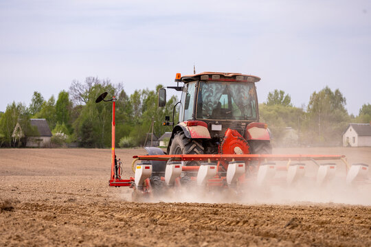 Tractor seeding soil with planter in agricultural field. Tractor drilling seeding crops at farm field. Agricultural activity. Tractor is equipped with seed planters to cultivate soil.
