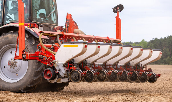 Precision inline seeder. A row seeder. Seed drill. Tractor with mounted seeder performing direct seeding of crops on plowed agricultural field. Farmer is using farming machinery for planting process.
