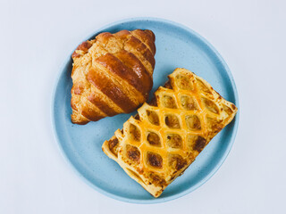 Fresh croissant and golden lattice puff pastry served on a blue plate against a clean white background, studio food photography ideal for bakery, breakfast, caf&eacute; menu, and pastry concepts.