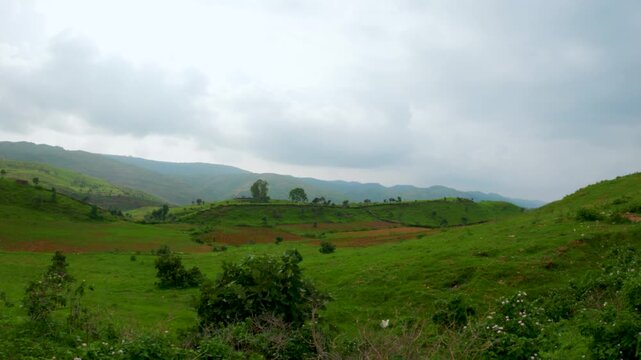 4K view of green Sahyadri hills as seen from moving vehicle at Rayta village, Udaipur, India. Green trees and grass on hills and clouds in sky during monsoon season. Road trip, travel and vacation con