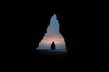 Silhouette of a person standing at a cave entrance, viewing a sunset