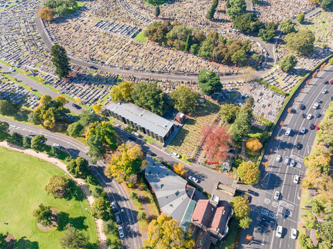 Aerial view of a Autumn coloured trees lining a busy road and sports oval alongside a city cemetary