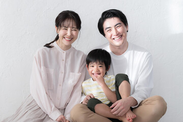 白い壁によりかかり、幸せが伝わる笑顔のファミリーポートレートカメラ目線の笑顔