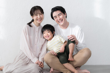 白い壁によりかかり、幸せが伝わる笑顔のファミリーポートレートカメラ目線の笑顔