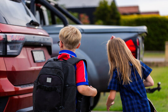 Boy and girl schoolkids putting backpacks into car ready  for trip to school