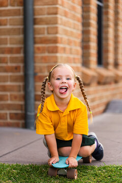 Young child in uniform riding around on penny board playing on driveway