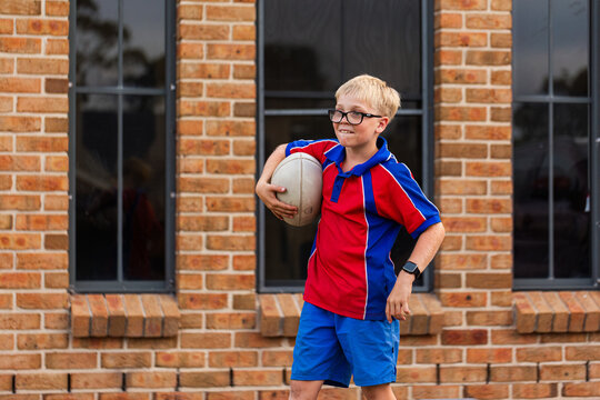 Australian schoolboy playing with ball in suburban front yard on overcast day after school