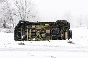 A yellow off road vehicle lies overturned on a snowy roadside during a heavy winter storm requiring emergency recovery services