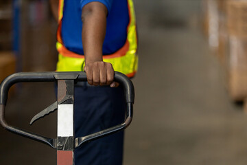Close-up of warehouse worker hand holding pallet jack handle, representing manual handling, warehouse equipment, and operational workflow in logistics and supply chain.