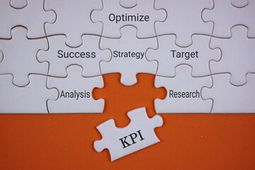white puzzle labeled KPI, linking strategy, analysis, target, optimization, and research to drive success. isolated on an orange surface.