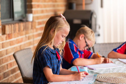 Australian school children siblings working on bookwork homework outside on back verandah