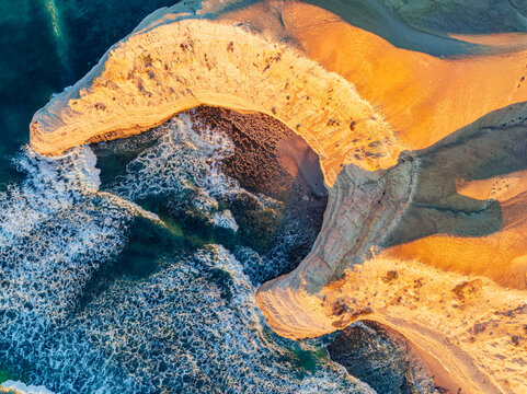 Aerial view of a crescent shaped cove along a rugged eroded coastline on golden evening light