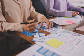 Close up ux developer and ui designer brainstorming about mobile app interface wireframe design on table with customer breif and color code at modern office.Creative digital development agency.