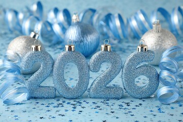 Sparkling blue 2026 numbers surrounded by festive ornaments and ribbons on a soft blue background, creating a joyful atmosphere for New Year celebrations