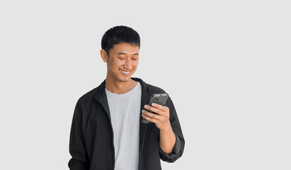 A young man happily looking at his smartphone isolated on a grey background. The concept of social media use