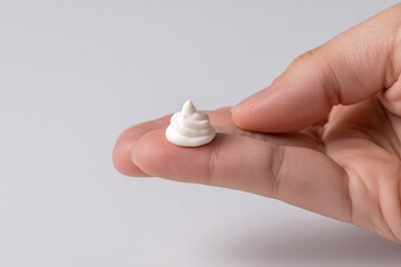 Hand holding a small dollop of white cream, showcasing smooth texture and shape, emphasizing skincare product application and personal care routine