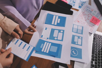 Close up ux developer and ui designer brainstorming about mobile app interface wireframe design on table with customer breif and color code at modern office.Creative digital development agency.