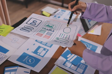 Close up ux developer and ui designer brainstorming about mobile app interface wireframe design on table with customer breif and color code at modern office.Creative digital development agency.