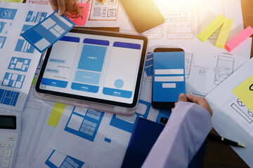 Close up ux developer and ui designer brainstorming about mobile app interface wireframe design on table with customer breif and color code at modern office.Creative digital development agency.