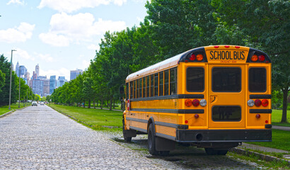 Yellow school bus parked on a city road. School transportation vehicle. Classic yellow school bus in a summer city. School bus waiting along a quiet road in an urban park.