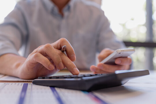 businessman using calculator and smartphone while analyzing financial data on paper documents, focusing on expense tracking and budgeting in office workspace. - Powered by Adobe