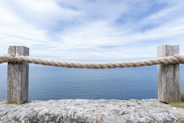 Rope barrier and stone wall overlooking calm ocean at coastal location under blue sky in daylight