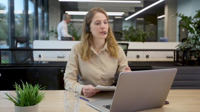 Friendly female helpline operator in call center. Young woman working in call center and holding microphone on headset with hand.