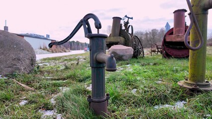 Old hand water pump standing on grass near vintage agricultural machines displayed outdoors