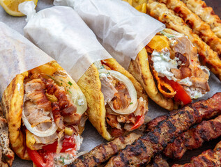 Gyro sliced meat pita bread wraps, pork skewers, and kebab, traditional greek food platter, closeup