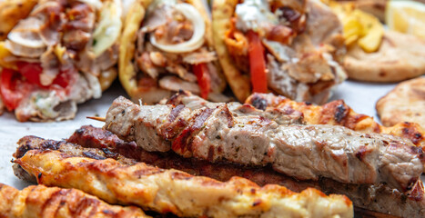 Mixed grilled meat platter, meat skewers, kebab pieces, and blur gyro wraps background, closeup