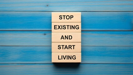 Motivational quote 'Stop Existing And Start Living' on wooden blocks, symbolizing personal growth, action, and a vibrant life on blue wood.