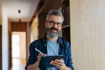Man standing by the window with tablet and writing notes.