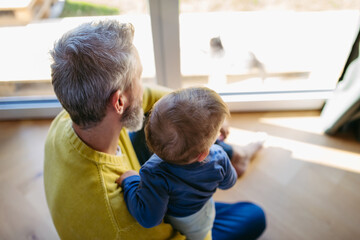 Father with little toddler son looking out of window.