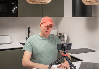 Backstage scene of a man recording vlog content at home while speaking to a smartphone mounted on a