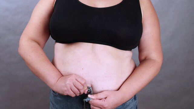 Woman in black tank top is adjusting her jeans, showing a gradual action of fastening and securing the waistband, highlighting the clothing fit and body movement