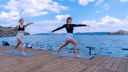 Women practicing yoga on a dock by the ocean in beautiful sunny weather
