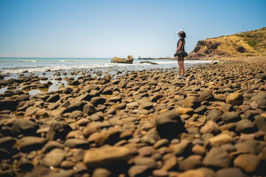 Side view of woman standing on the beach against clear sky, gazing into the ocean, with pepples in the foreground, Hallet Cove, Adelaide, South Australia, Australia