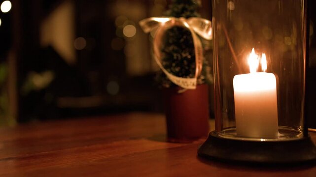 White Pillar Candle Burning in Glass Lantern on Wooden Table