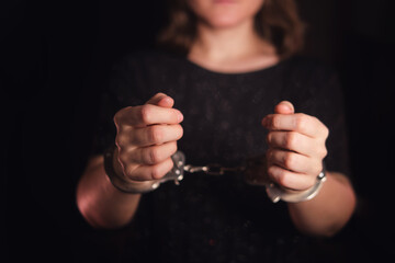 Woman in dark clothes with hands handcuffed. Concept of arrest, crime, justice, punishment, or human rights violation.