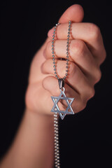 Woman holding silver star of David necklace on a chain. Religious symbol of Judaism for spirituality and faith in God.