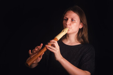 Woman playing a recorder on a black background. Female musician performing classical music. Instrument practice and musical education concept.