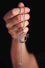 Woman holding a silver pendant with crescent moon and star symbol. Spirituality concept for worship and religious holidays.
