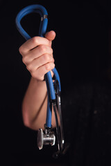 Woman hand holding a blue stethoscope against a dark background, representing healthcare and medical profession. Doctor instrument for diagnosis.
