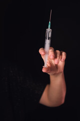 Woman holding a medical syringe with needle on a black background. Healthcare, vaccination, and drug addiction concept.