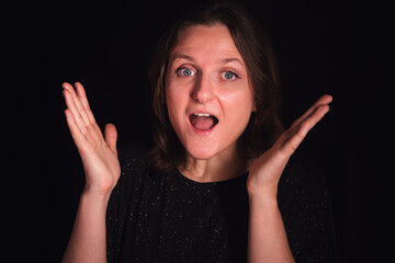 Woman with wide eyes and open mouth showing surprise or shock against a dark background. Emotional expression for advertising and social media.