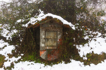 Rustic winter scene featuring an abandoned small stone structure surrounded by frozen vegetation and deep white snow in the countryside
