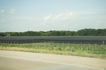 Rows of solar panels in grassy field beside rural highway